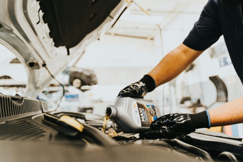 Close-up of a mechanic pouring engine oil in a car inside a garage. Hands wearing gloves.